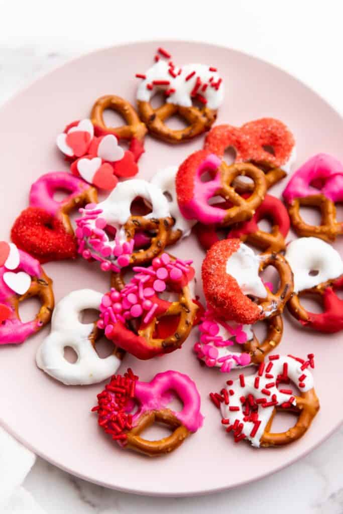 Overhead view of a plate of Valentine's themed dipped pretzels with sprinkles. 