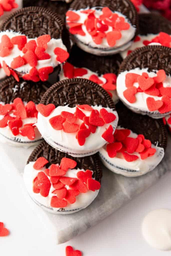 Close up of a pile of oreo cookies, half dipped in white candy melts, with candy heart sprinkles. 