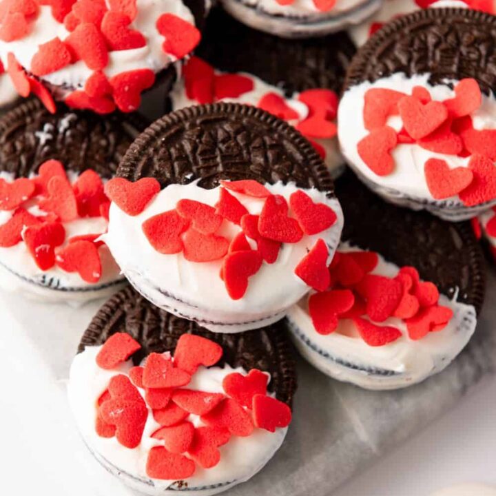 Close up of a pile of oreo cookies, half dipped in white candy melts, with candy heart sprinkles.