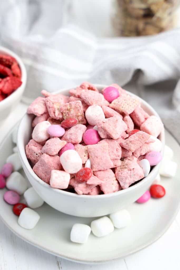 Close up of a small bowl of Valentine's Day Puppy Chow snack,  with strawberry, white chocolate covered Chex cereal, M&Ms and mini marshmallows. 