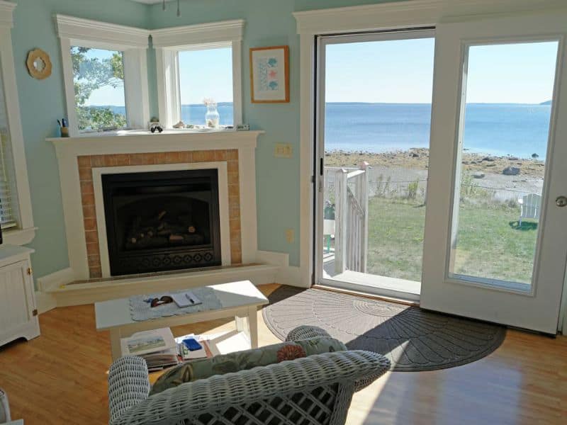 Cozy livingroom with fireplace, with large windows showing Maine's oceanfront coast. 