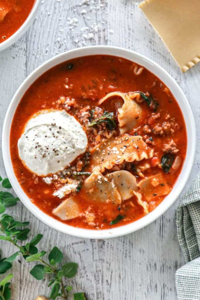 One pot lasagna soup with ground beef spinach and pieces of lasagna noodles is served in a rich tomato broth. A generous scoop of cottage cheese and grated Parmesan top the hearty soup.