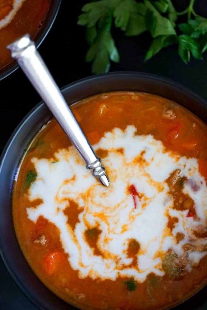 Bowl of turkey lentil soup with metal spoon and cocnut milk swirled on top.