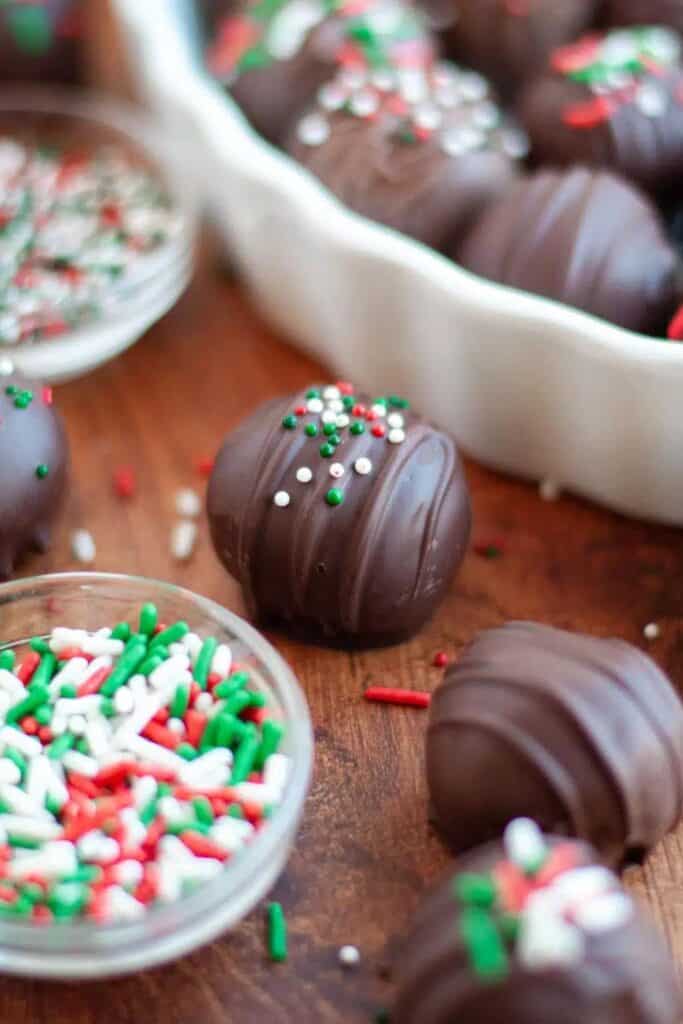 Close up of three oreo truffle balls, covered in milk choclate and Christmas sprinkles. 