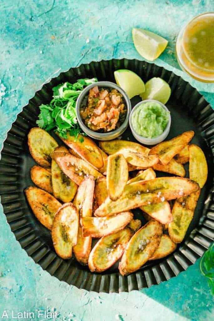 Plate of oven baked plantains with two small dip bowls of salsa. 