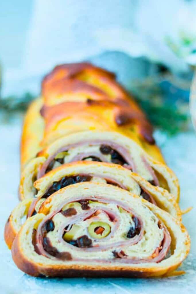 lices of Venezuelan ham holiday bread are arranged in front of the remaining golden baked loaf. Each spiral slice reveals layers of ham, green olives, and dark raisins rolled inside the soft bread.