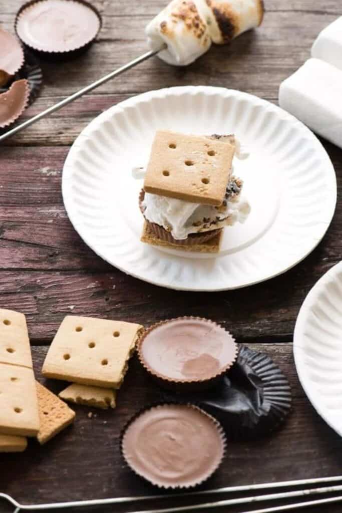 Paper plate with peanut butter cup s'mores beside a roasting stick with two roasted marshmallows. 