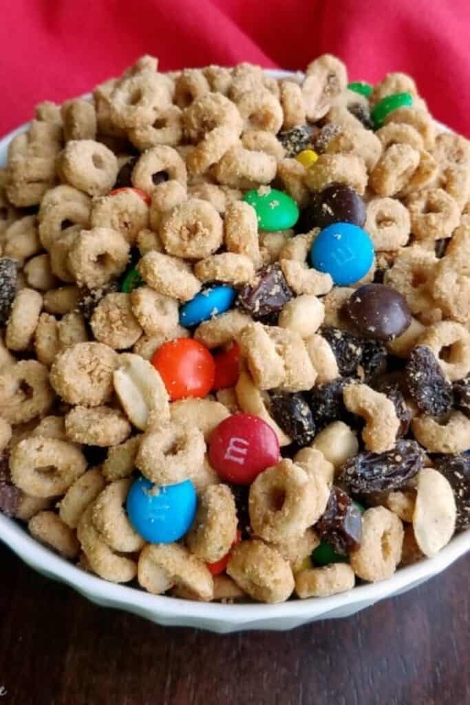 Bowl of sweet snack mix made with toasted oat cereal rings, chocolate candies, raisins, peanuts, and chocolate chunks.