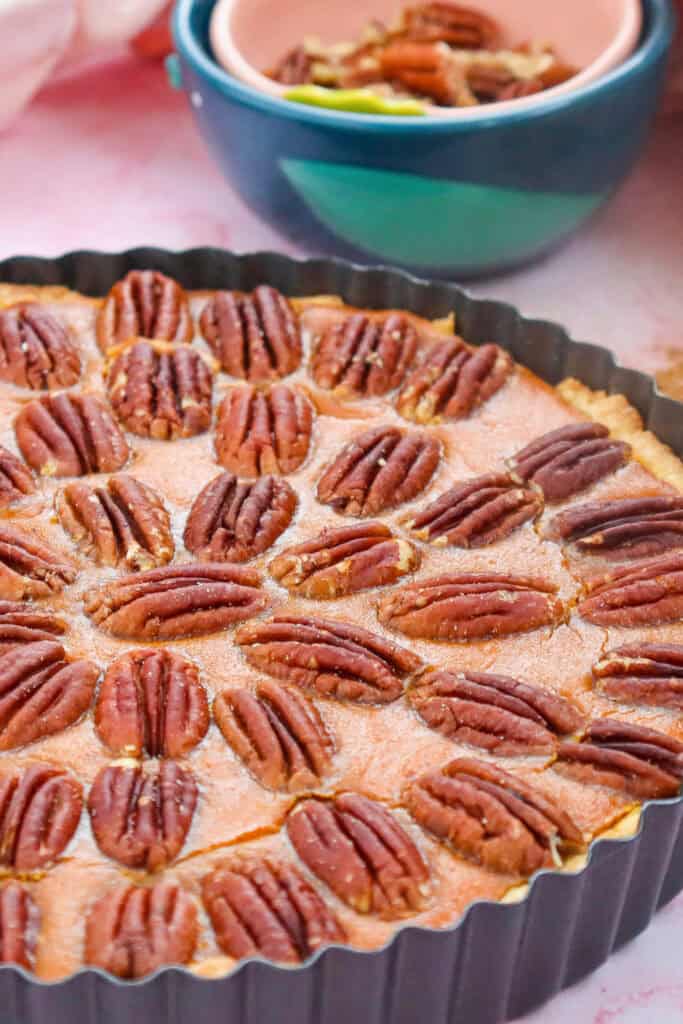 Close-up of a pecan pumpkin cheesecake pie with creamy pumpkin filling in a golden crust, topped with whole pecans and baked in a fluted tart pan.