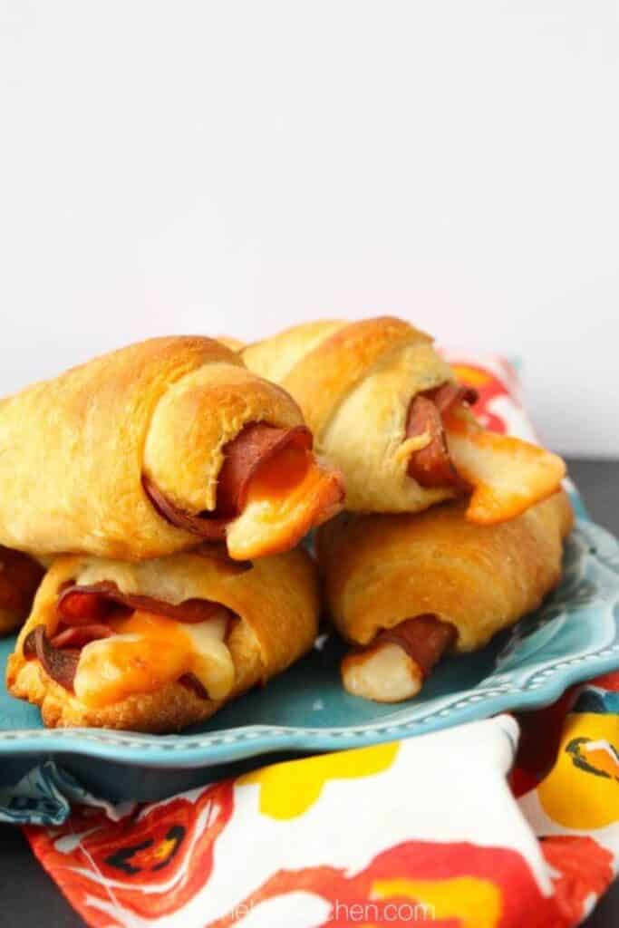 Pizza stuffed crescent rolls baked until golden and filled with melted cheese and pepperoni slices. The warm rolls sit stacked on a blue plate with cheese stretching from the centers.
