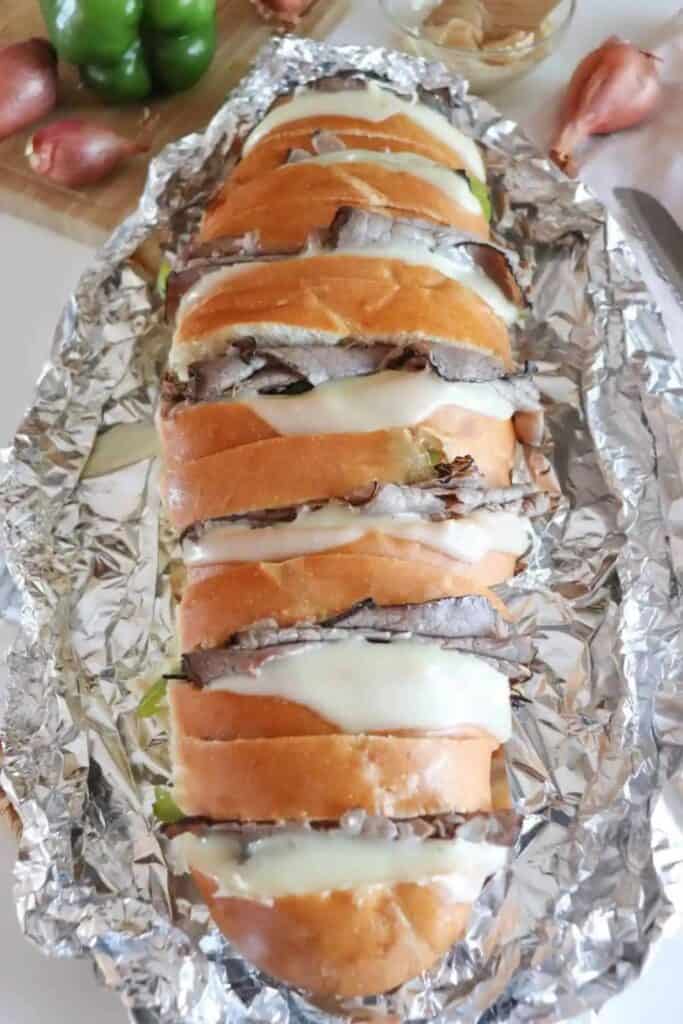 Philly Cheesesteak baguette cut into slices, oozing melted cheese on a piece of tinfoil. 