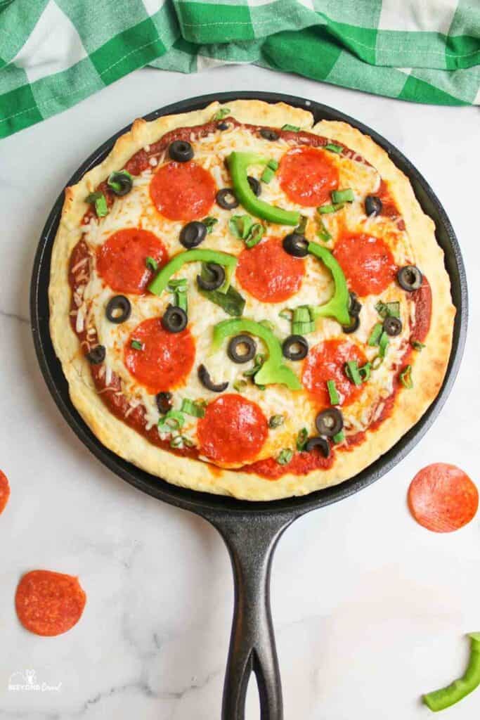 Pizza with pepperoni, green pepper, and black olives in a cast iron pan.