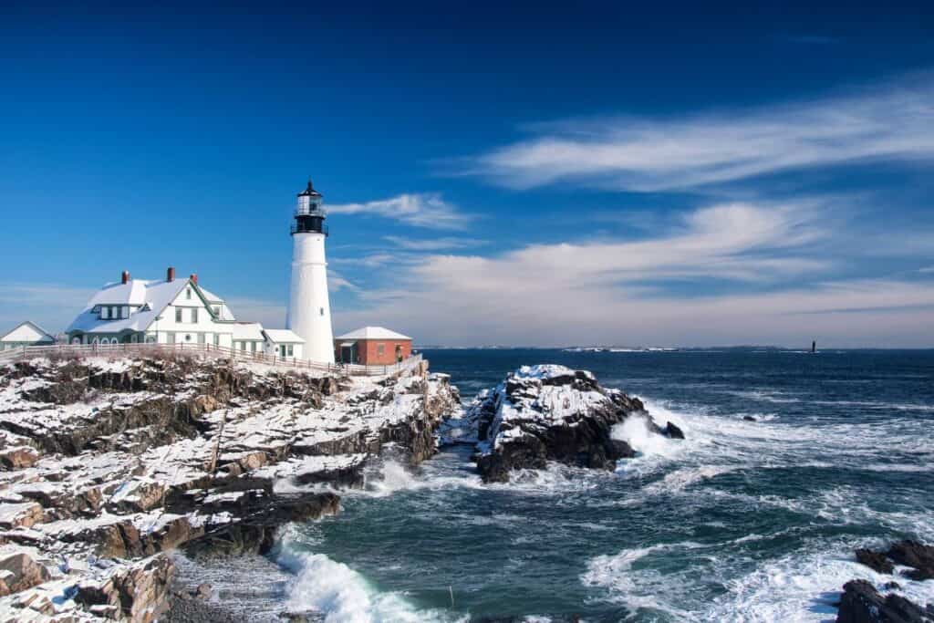 Rocky winter Maine shore and Lighthouse dusted in snow. 