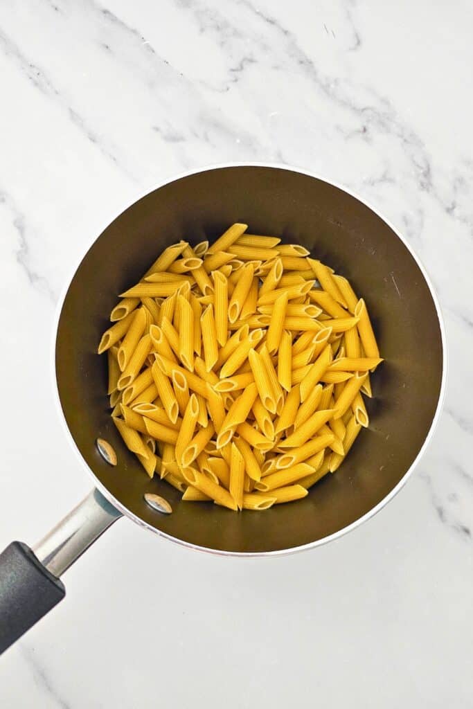 Overhead view of a pot of uncooked penne pasta on a marbled surface.