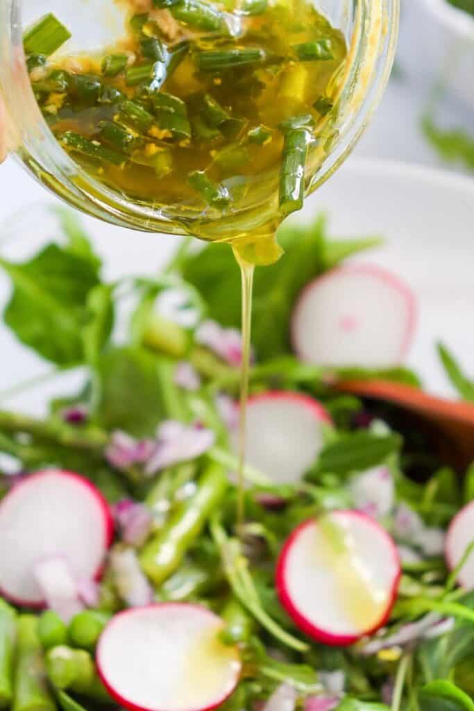 Pouring the lemon salad dressing over the cod asparagus salad in a clea serving bowl. 