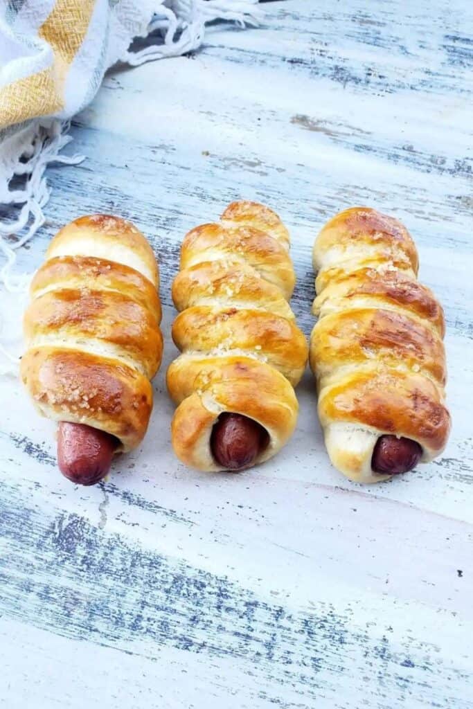 Three Pretzel dogs made with hot dogs wrapped in dough on a plate. 