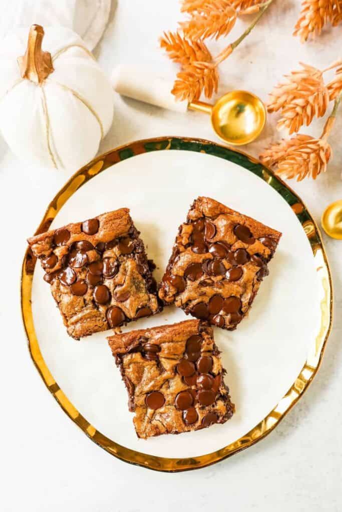 Three pumpkin chocolate chip bars on a fancy plate, beside a white & gold pumpkin.