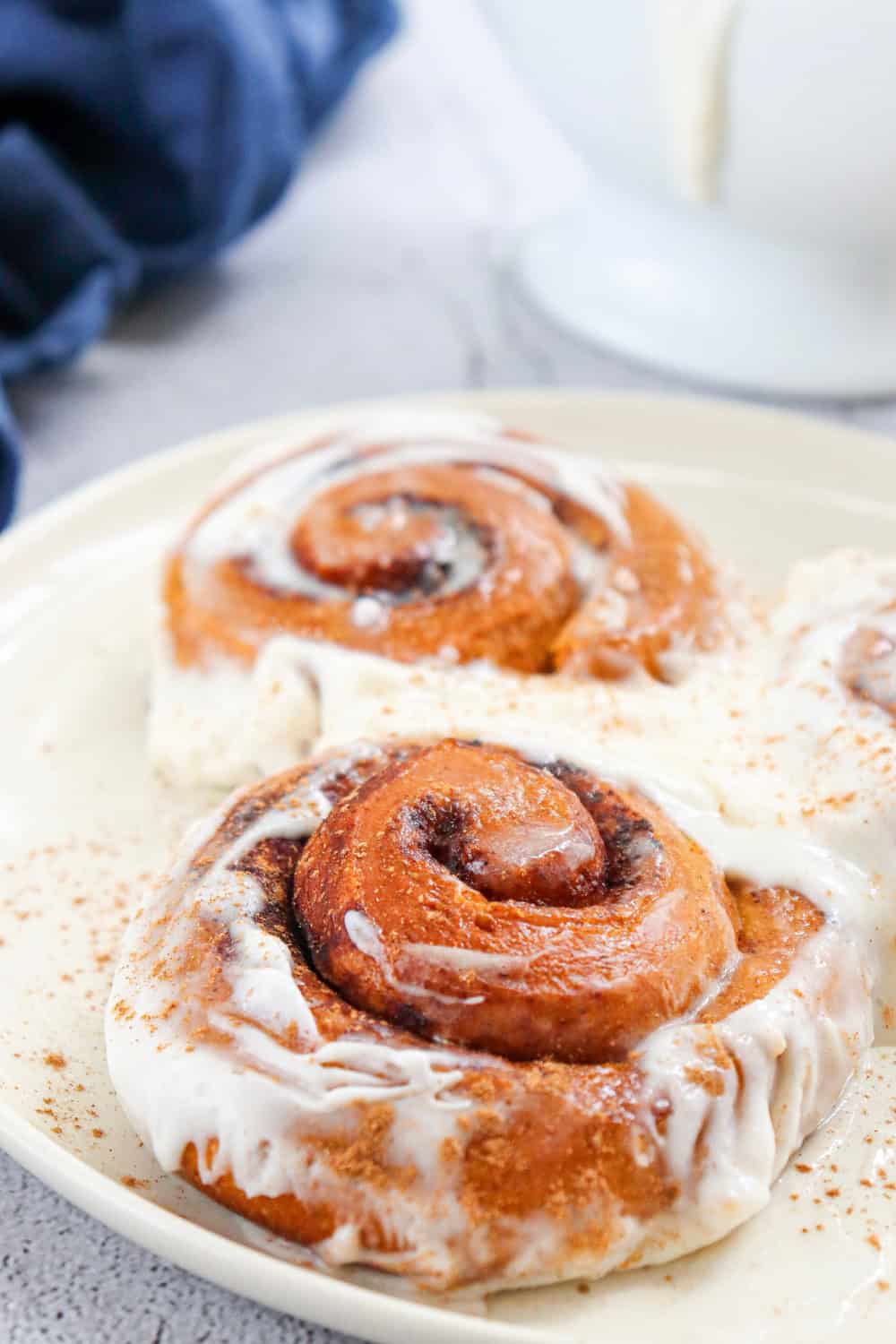 Close up of pumpkin cinnamon rolls with warm cinnamon swirls covered in maple cream cheese icing and a light dusting of cinnamon.
