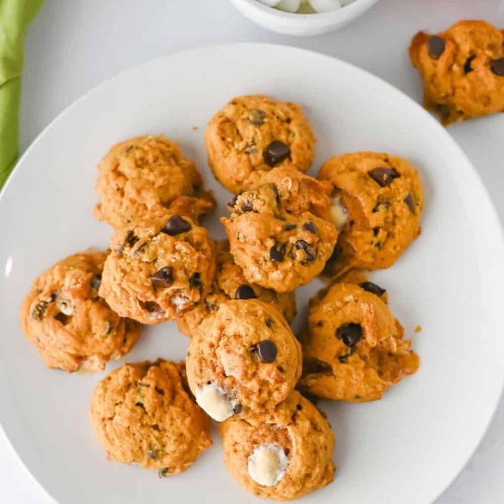 An overhead view of a plate of pumpkin s'mores cookies with visible chocolate chips and mini marshmallows.