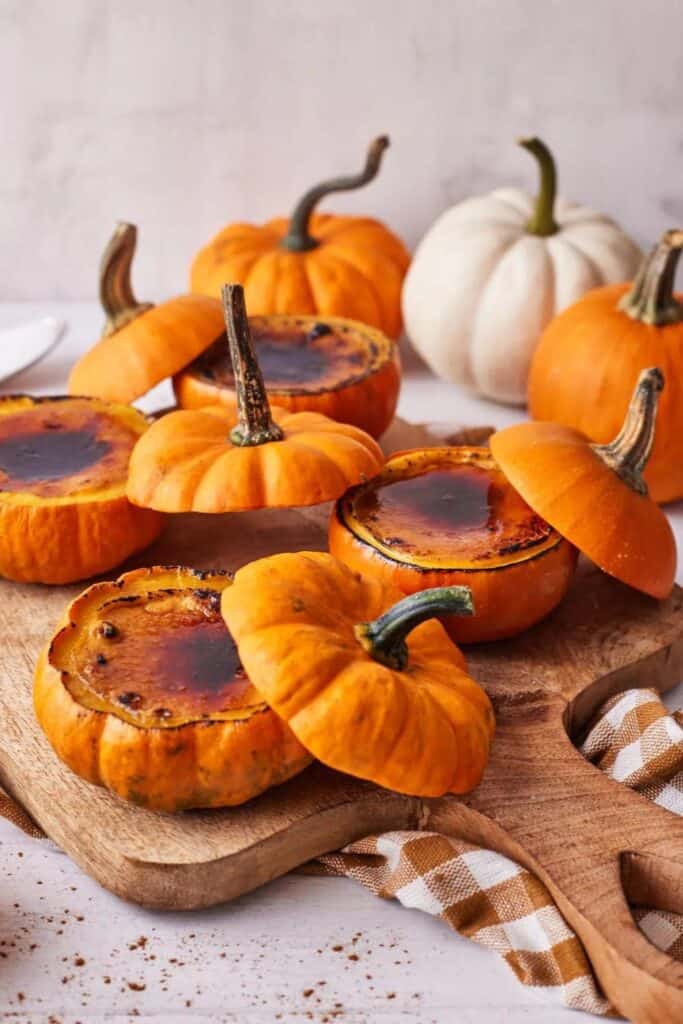 Small cooked mini pumpkins filled with  pumpkin creme brulee on a wooden cutting board. The ultimate fall pumpkin dessert. 