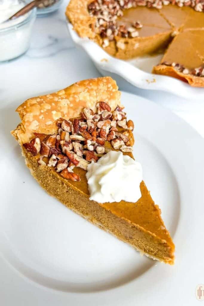 Slice of pumpkin custard pie otopped with whipped cream and pieces of pecans. 