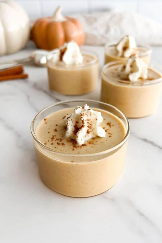 4 clear bowls of pumpkin panna cotta autumn dessert topped with whipped cream and pumpkin spice. 