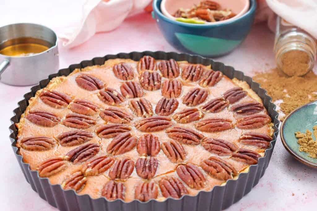 A whole Pecan Pie Pumpkin Cheesecake in a scapploped dish,  with a rich pumpkin filling, topped with crunchy pecans, perfect for a fall dessert like Pumpkin Pecan Cheesecake.