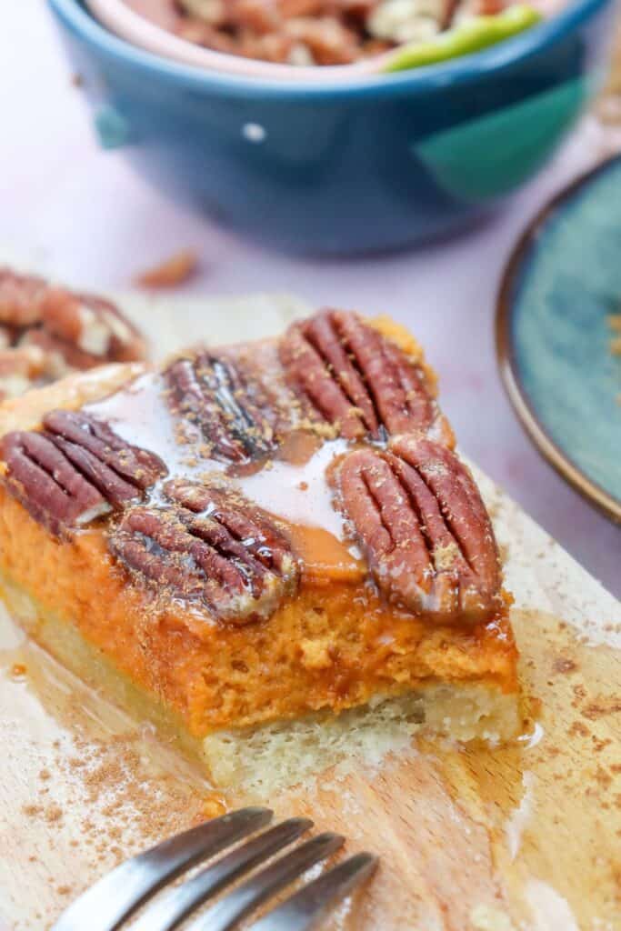 A closeup of a slice of pumpkin pie cheesecake topped with pecans. 