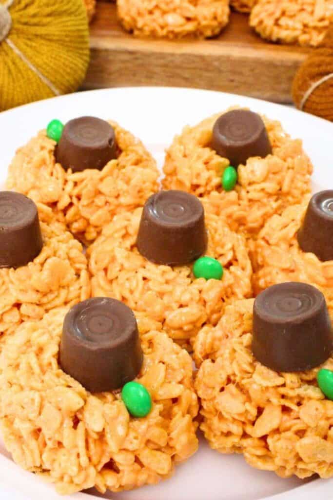 umpkin Rice Krispie treats shaped into round orange pumpkins with chocolate candy centers and small green candy stems. The no bake treats are arranged together on a white serving plate.