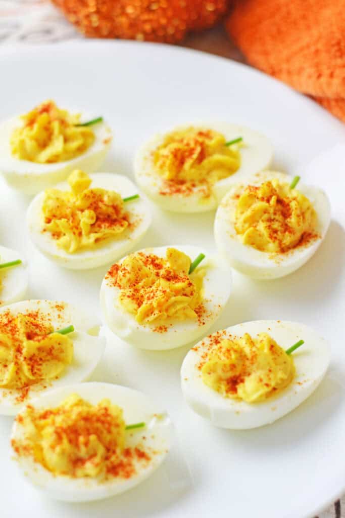 Pumpkin deviled eggs with creamy yellow filling dusted with paprika and topped with small chive stems. The festive pumpkin shape makes them an easy Fall and holiday appetizer.