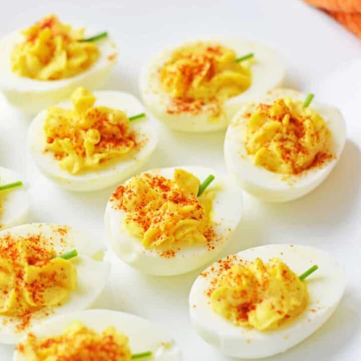 Pumpkin deviled eggs with creamy yellow filling dusted with paprika and topped with small chive stems. The festive pumpkin shape makes them an easy Fall and holiday appetizer.