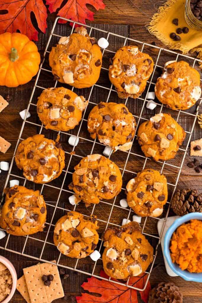 Rows of Pumpkin S'mores cookies with chocolate chips and marshmallows on a cooling rack. 