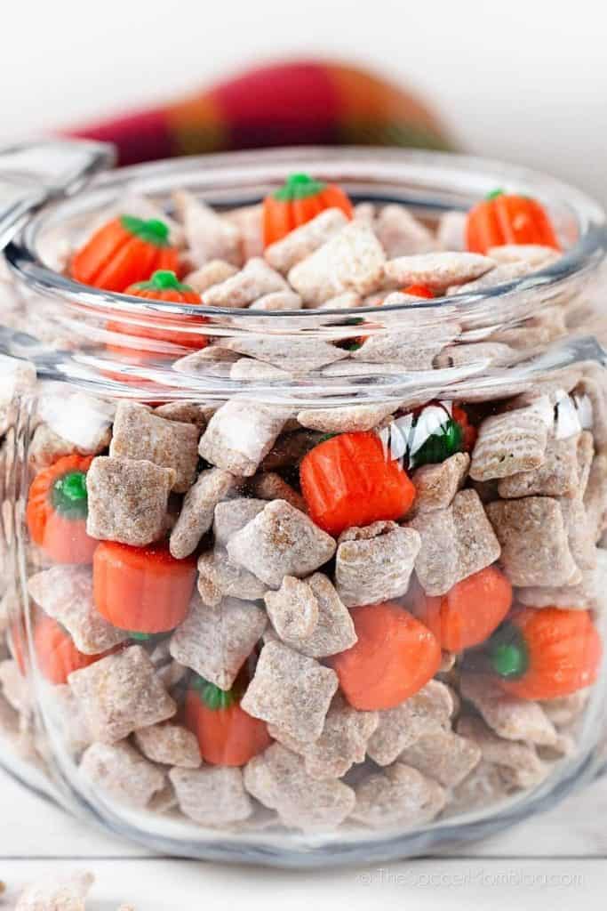 Glass jar filled with Pumpkin Spice Puppy Chow, a sweet snack mix made of powdered sugar-coated cereal pieces and candy pumpkins.