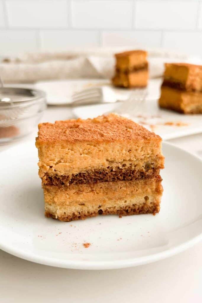 Square layered pumpkin dessert with creamy orange filling and darker spiced layers dusted with cinnamon on top. This chilled treat is an easy option for no bake Thanksgiving dessert ideas.