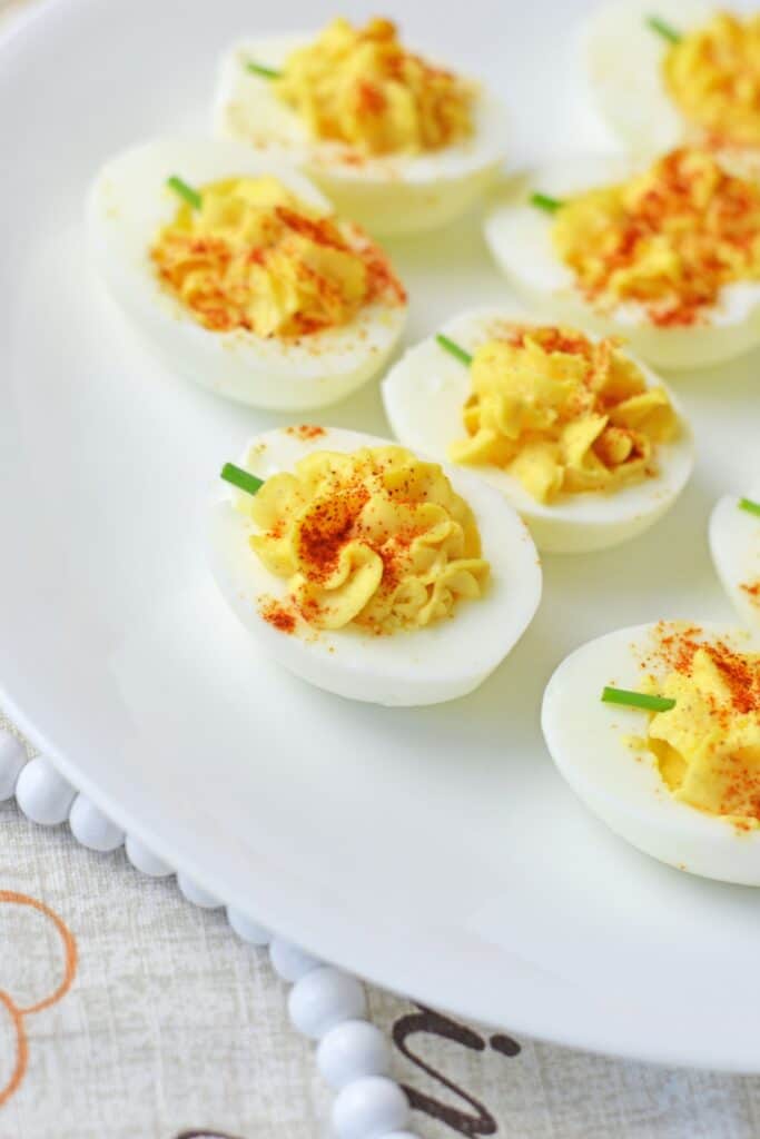 Pumpkin shaped deviled eggs with creamy yellow filling dusted with smoked paprika and topped with green chive stems. The individual portions make a festive finger food appetizer.