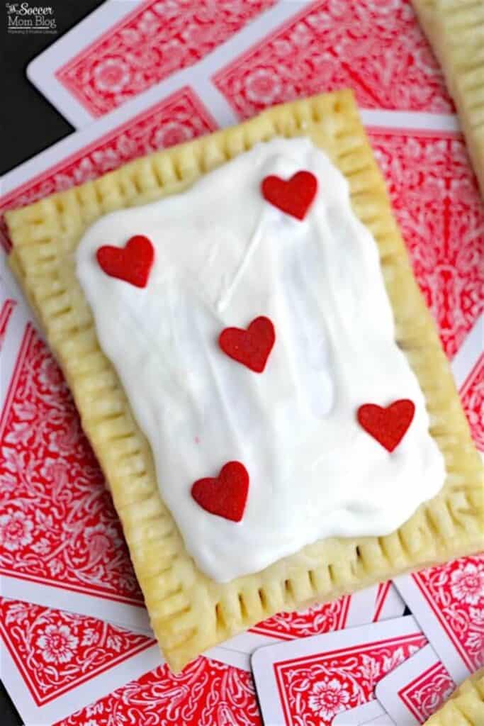 Hamoemade poptart with vanilla icing and 5 heart candies over playing cards. 