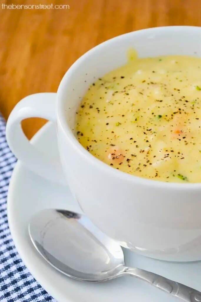 Chicken rice soup served in a white mug with tender chicken, rice, and vegetables in a creamy broth topped with cracked black pepper. The mug sits on a saucer with a spoon beside it showing a warm bowl of chicken rice soup for a last minute dinner.