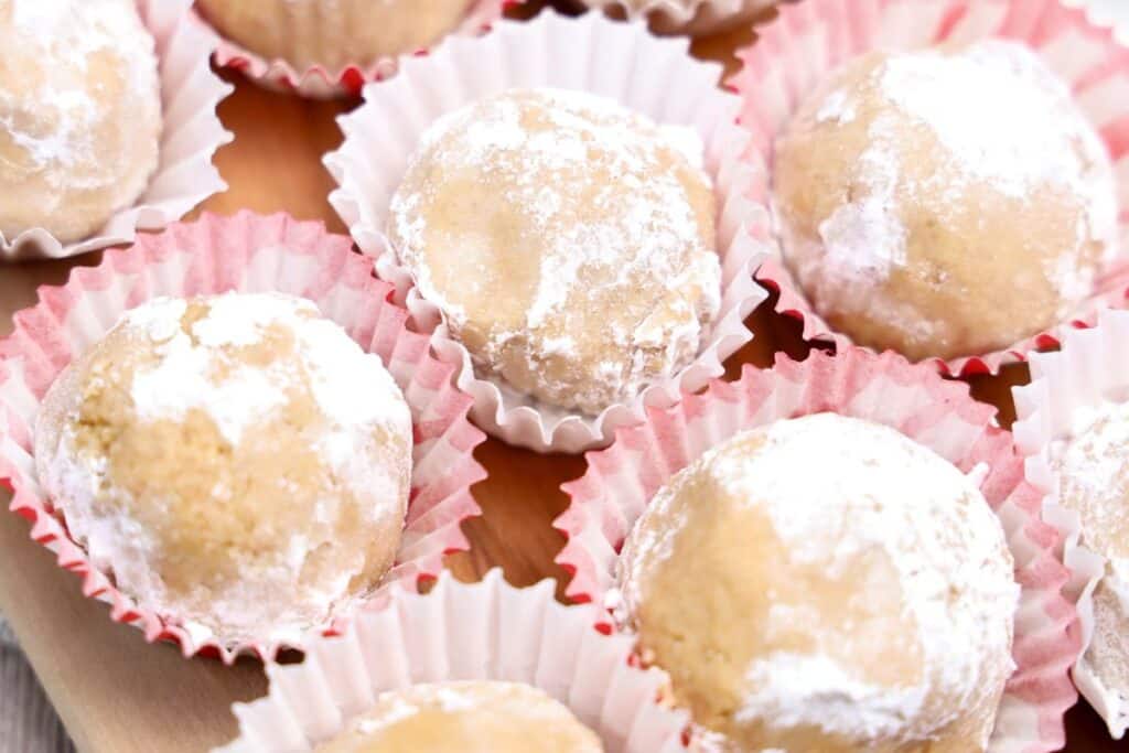 Close up of 6 peanut butter balls rolled in powdered sugar in cupcake liners on a wooden board. 