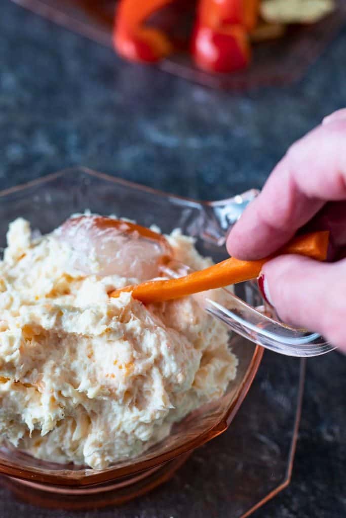 Creamy quick shrimp dip served in a glass bowl, with a carrot stick being dipped into the mixture. The dip has a light, fluffy texture with bits of shrimp.