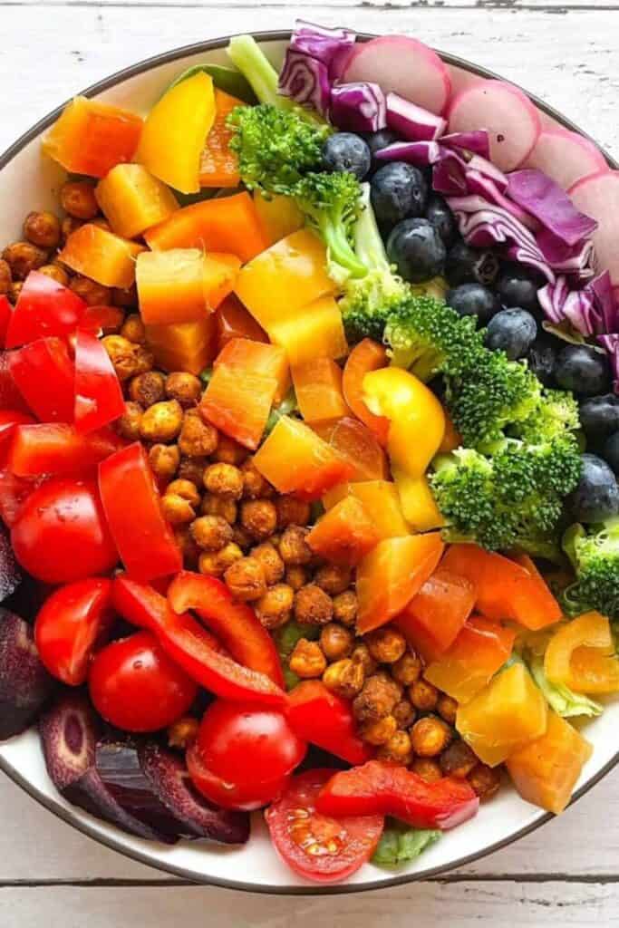 Bowl with side by siad layers or rainbow colored veggies & fruit.