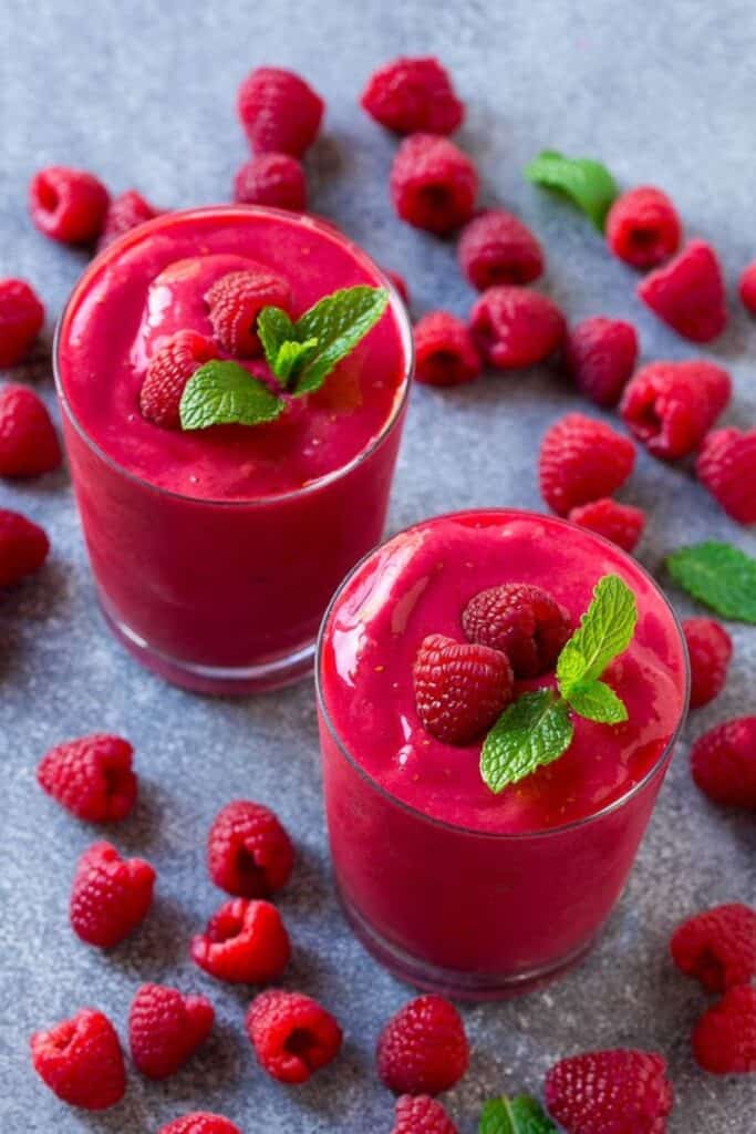Two glasses of Raspberry Smoothies with raspberries & mint sprigs on top