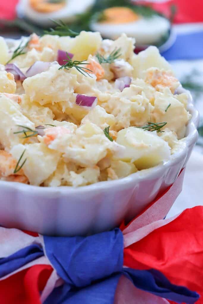 Close up of medium sized scalloped dish of red potato salad with red oinion, egg, mayo and fresh dill. 