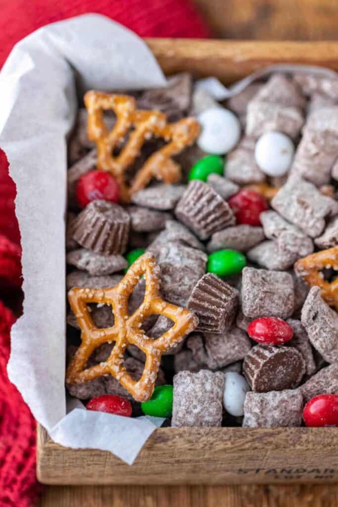 Wooden box filled with reindeer chow. A mix of chex cereal, holiday shaped pretzels, Christmas M&Ms and choco-peanut butter mini cups. 