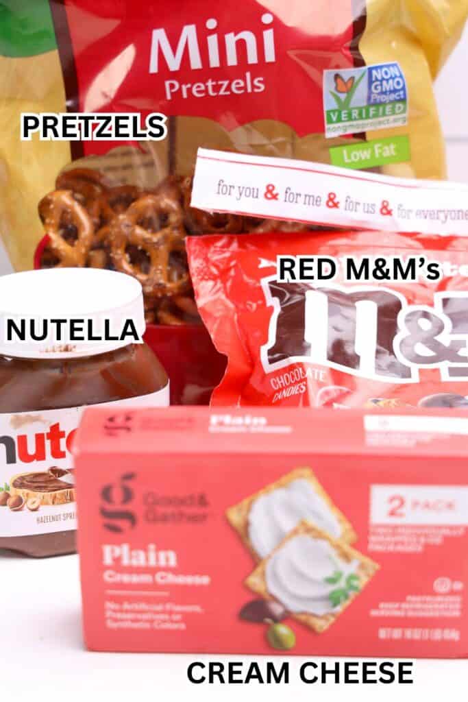 Ingredients for reindeer dip arranged together, including a bag of mini pretzels, a container of Nutella, red M&M’s, and a box of plain cream cheese.