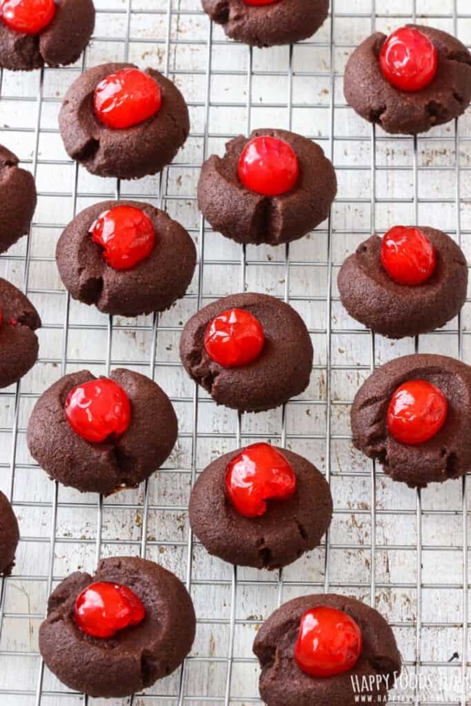 Chocolate thumbprint cookies are topped with glossy red maraschino cherries and arranged neatly on a wire cooling rack to look like Rudolph's Nose.