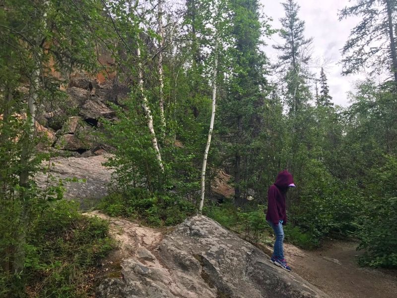 Picture of boreal forest. A Young girl is walking past  a rockfall, along the Cameron Falls Trail.