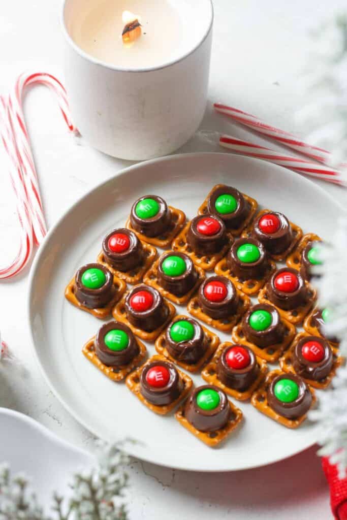 Plate of square pretzels, topped with one rolo and one Christmas colored M&M each.