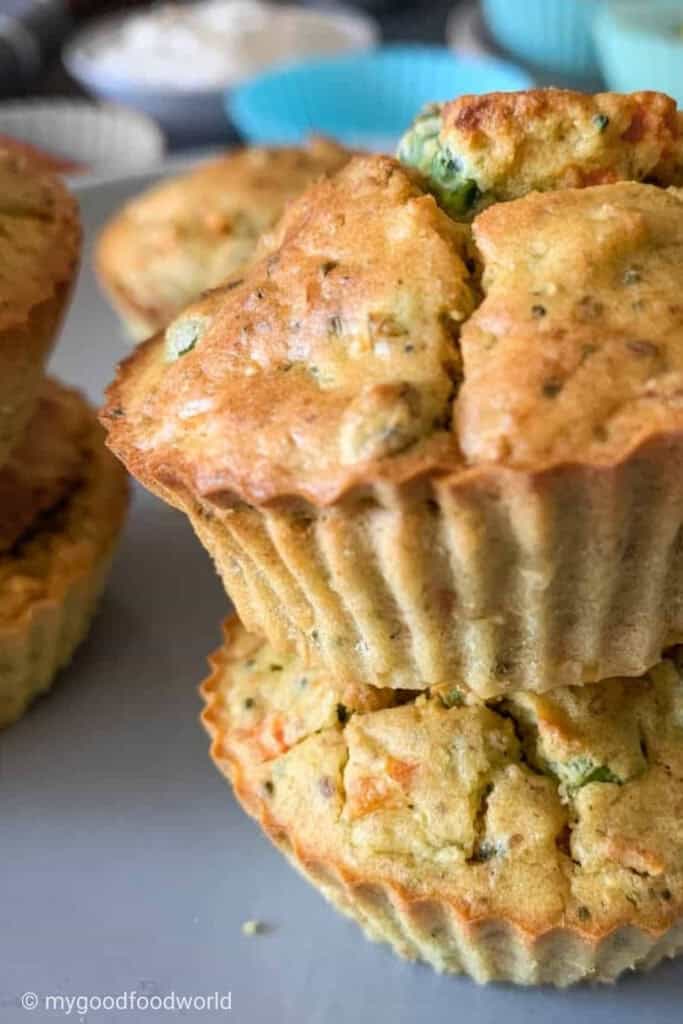 Stacked eggles and gluten-free savory veggie muffins baked in fluted silicone liners, featuring a golden crust with visible bits of carrot, spinach, and herbs.