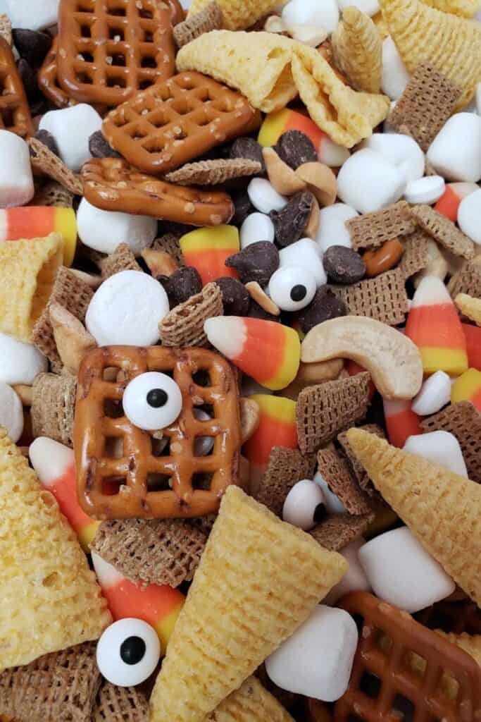 Halloween snack mix with candy eyes, candy corn, creeal and square pretzels. 
