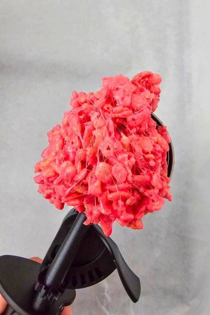 Close-up of a black ice cream scoop holding a sticky portion of bright red rice krispie mixture, ready to be shaped into Halloween treats.